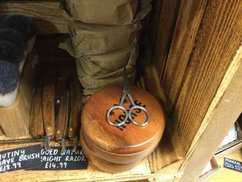 Stainless steel beard scissors on a wooden shelf.