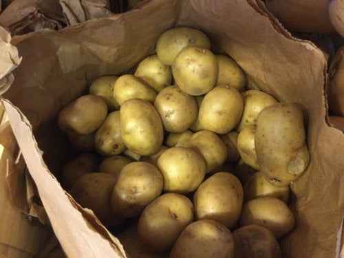 Organic white potatoes in a brown paper bag, showcasing their smooth texture.