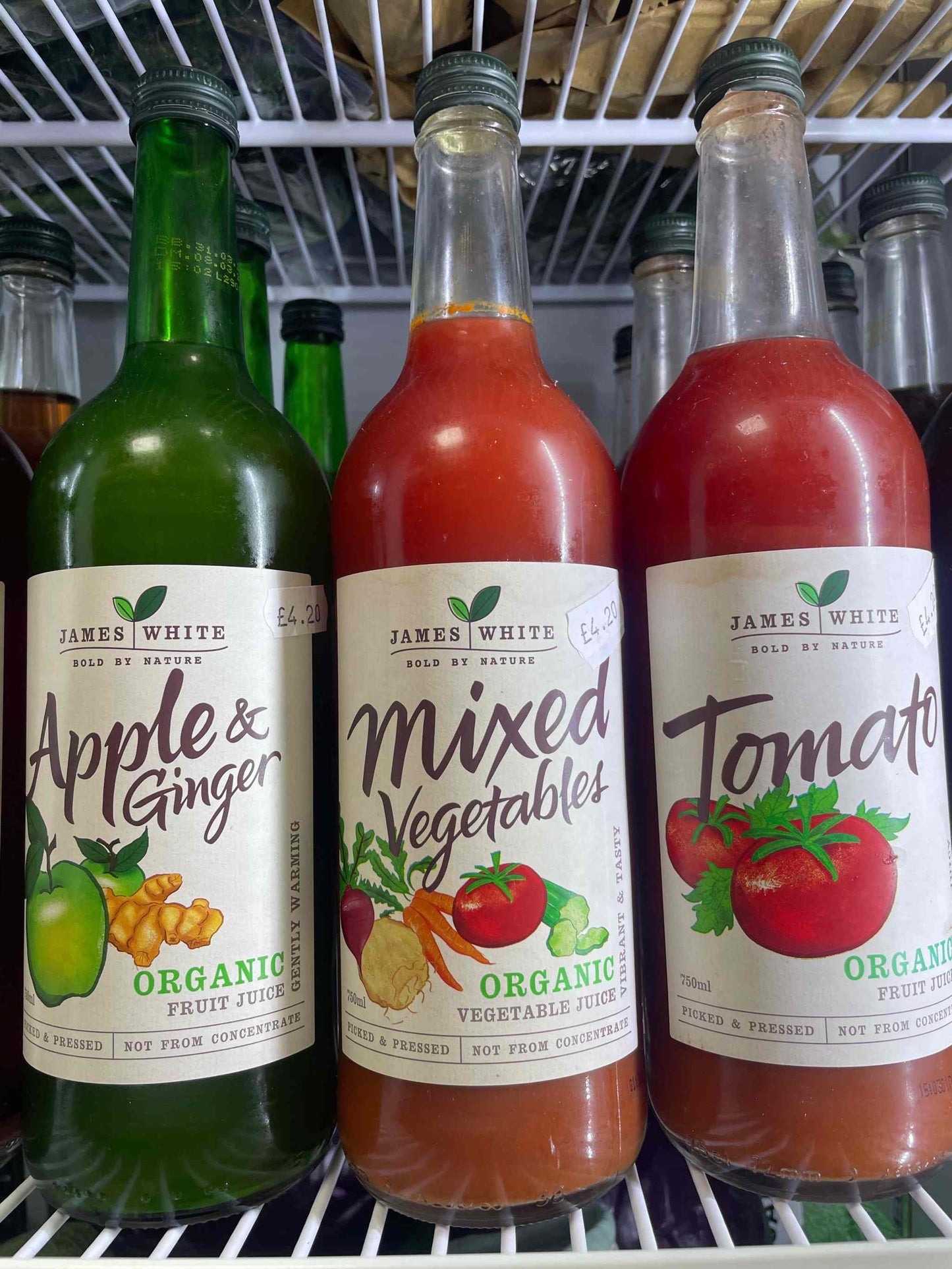 James White Juice bottles on a shelf, showcasing apple & ginger, mixed vegetables, and tomato flavors.