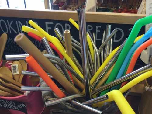 Eco-friendly single metal straws in a variety of colors, displayed in containers.