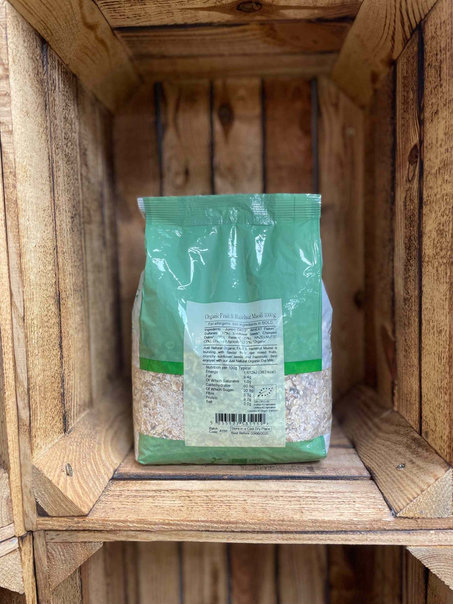 Organic Fruit and Hazelnut Muesli 1kg in green packaging, displayed in a wooden crate.