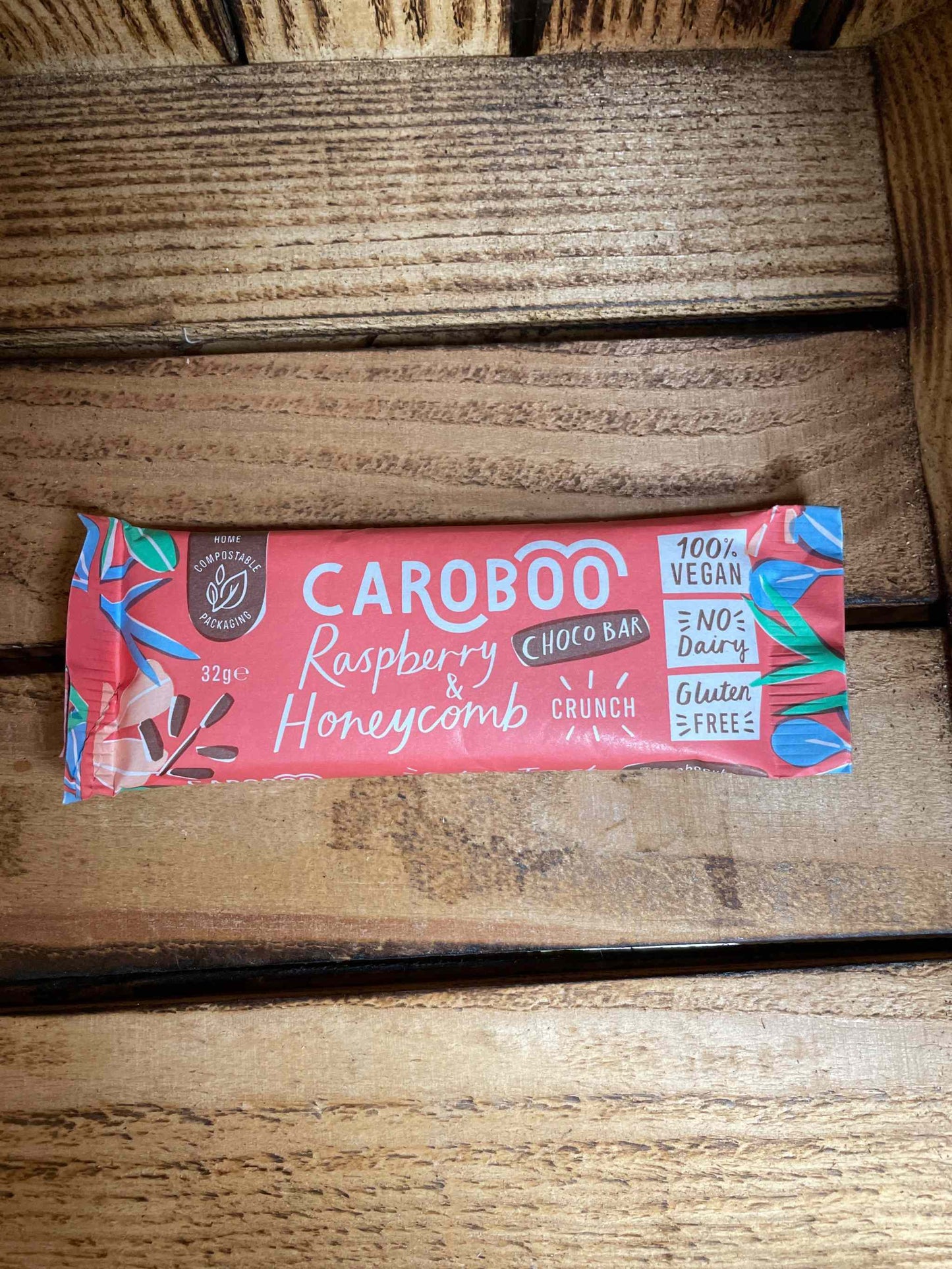 Carob Bar with Raspberry and Honeycomb in red packaging on wooden surface.