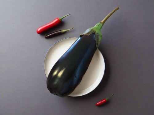 Organic aubergine on a white plate with red chili peppers.