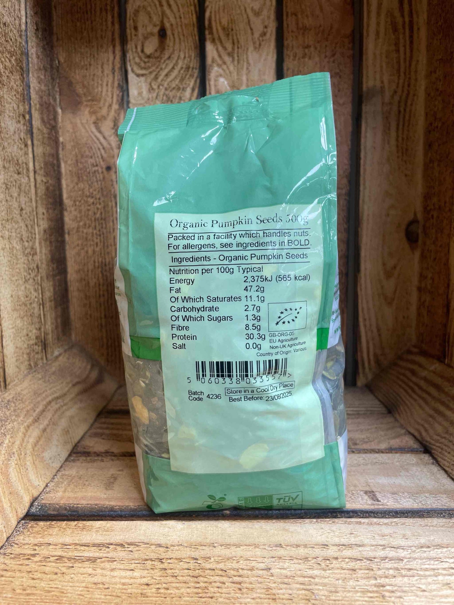 Organic pumpkin seeds 500g package on wooden shelf.