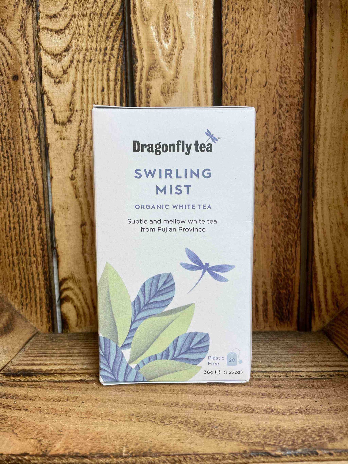 Swirling Mist Organic Tea box packaging with leaf and dragonfly design on a wooden background.
