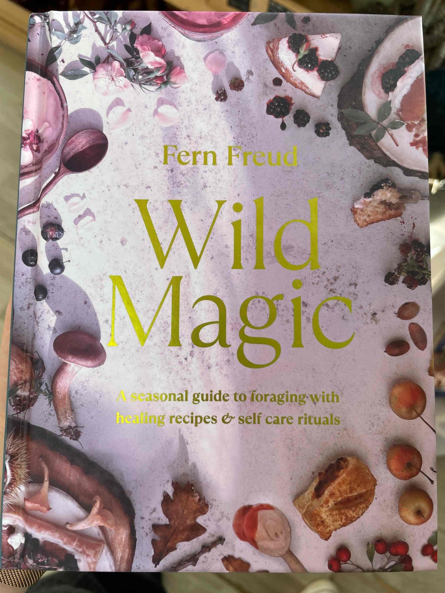 Cover of "Wild Magic" book with floral and fruit designs, featuring a guide to foraging and self-care rituals.