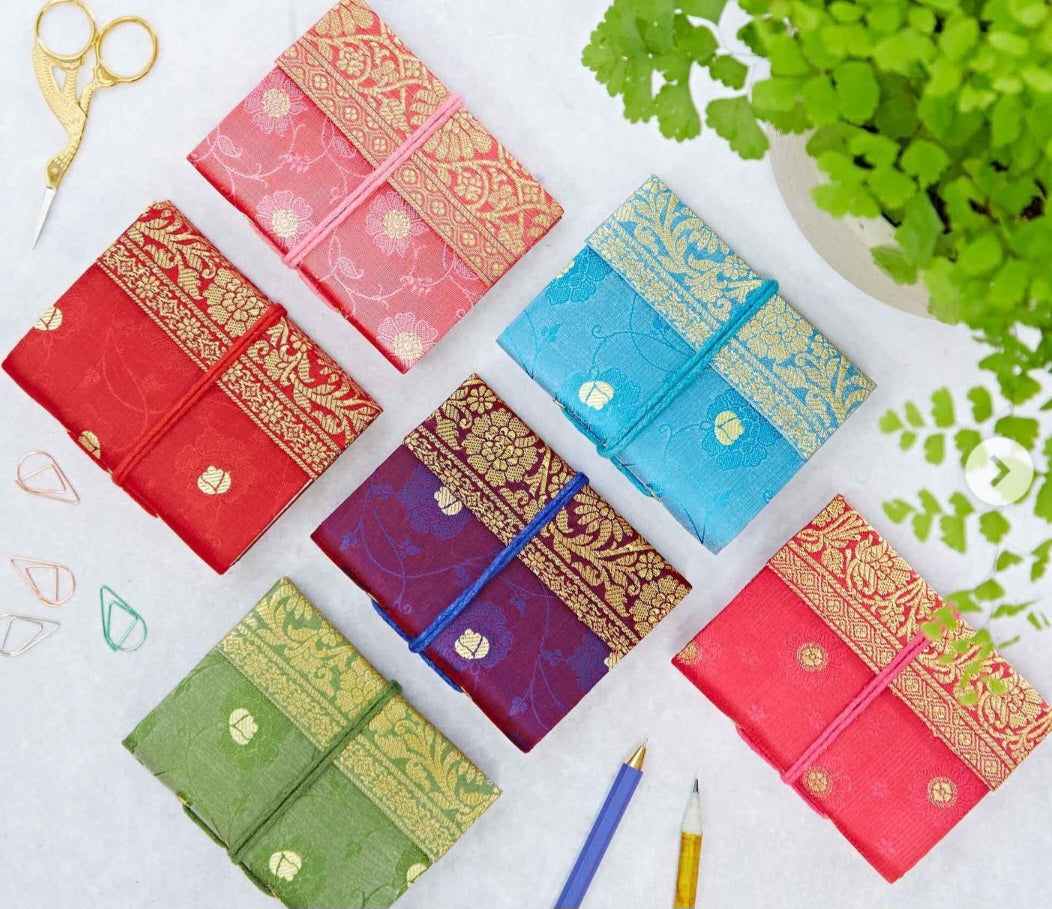 colorful recycled sari journals with intricate patterns displayed next to plant and stationery