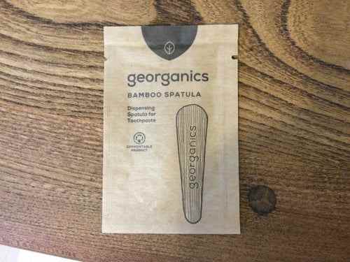 Eco-friendly bamboo toothpaste spatula in packaging on wooden surface.