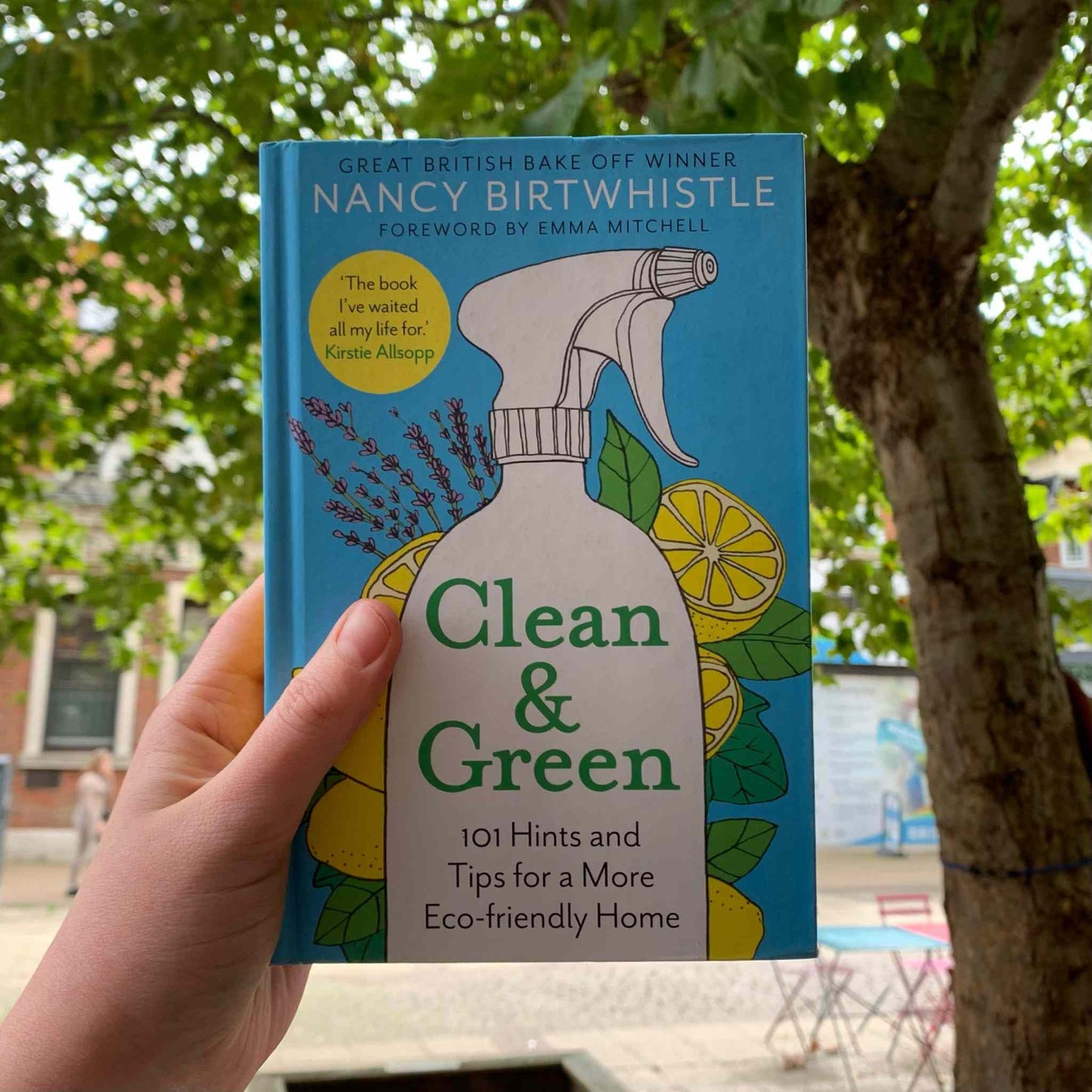 Clean & Green book by Nancy Birtwhistle held outdoors with trees and buildings in the background.