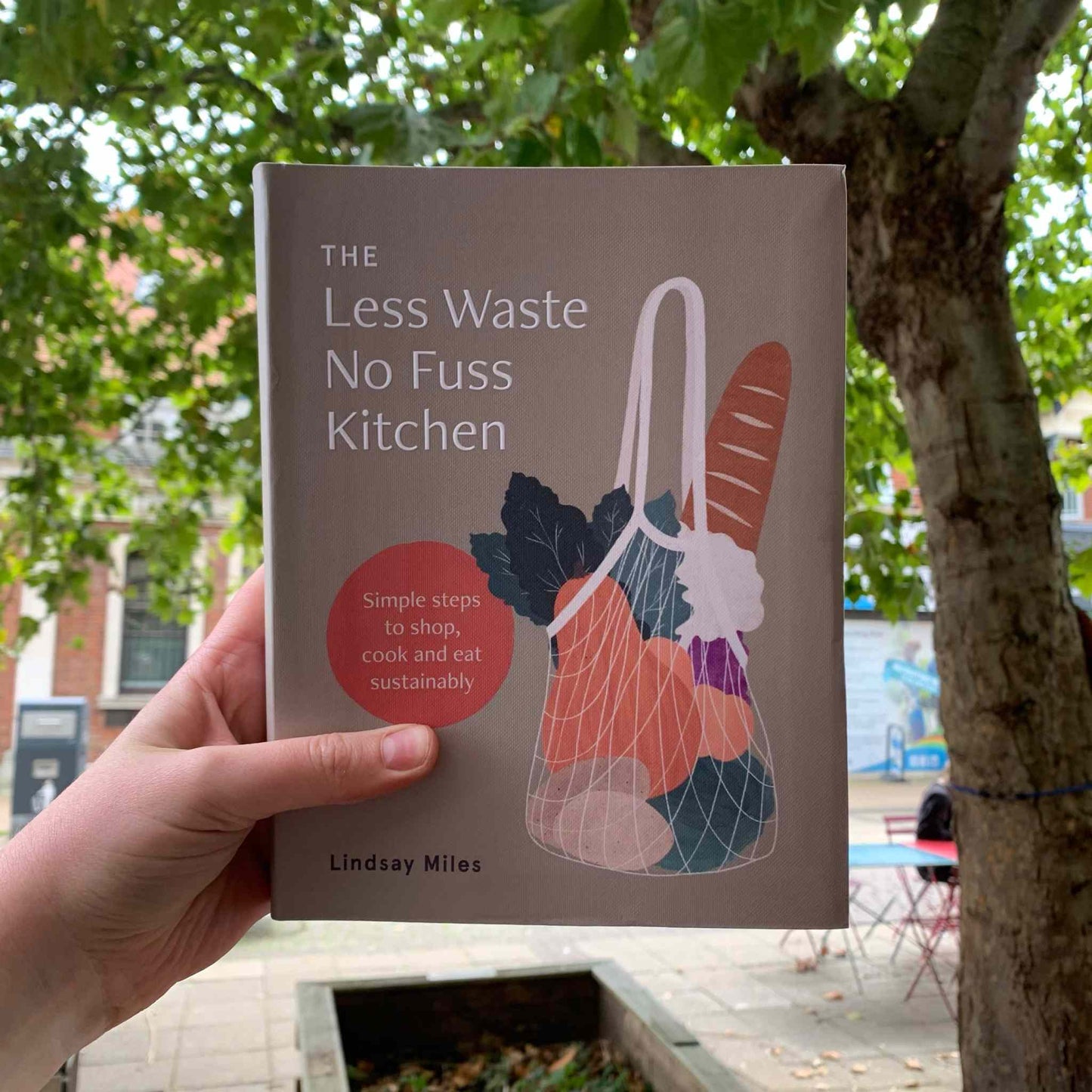 Less Waste, No Fuss Kitchen book by Lindsay Miles held outdoors, promoting eco-friendly kitchen tips.