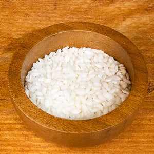 Arborio Rice (100g) in a wooden bowl on a wooden surface.