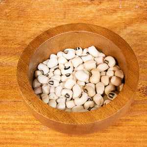 Black eye beans (100g) in a wooden bowl on a wooden surface.