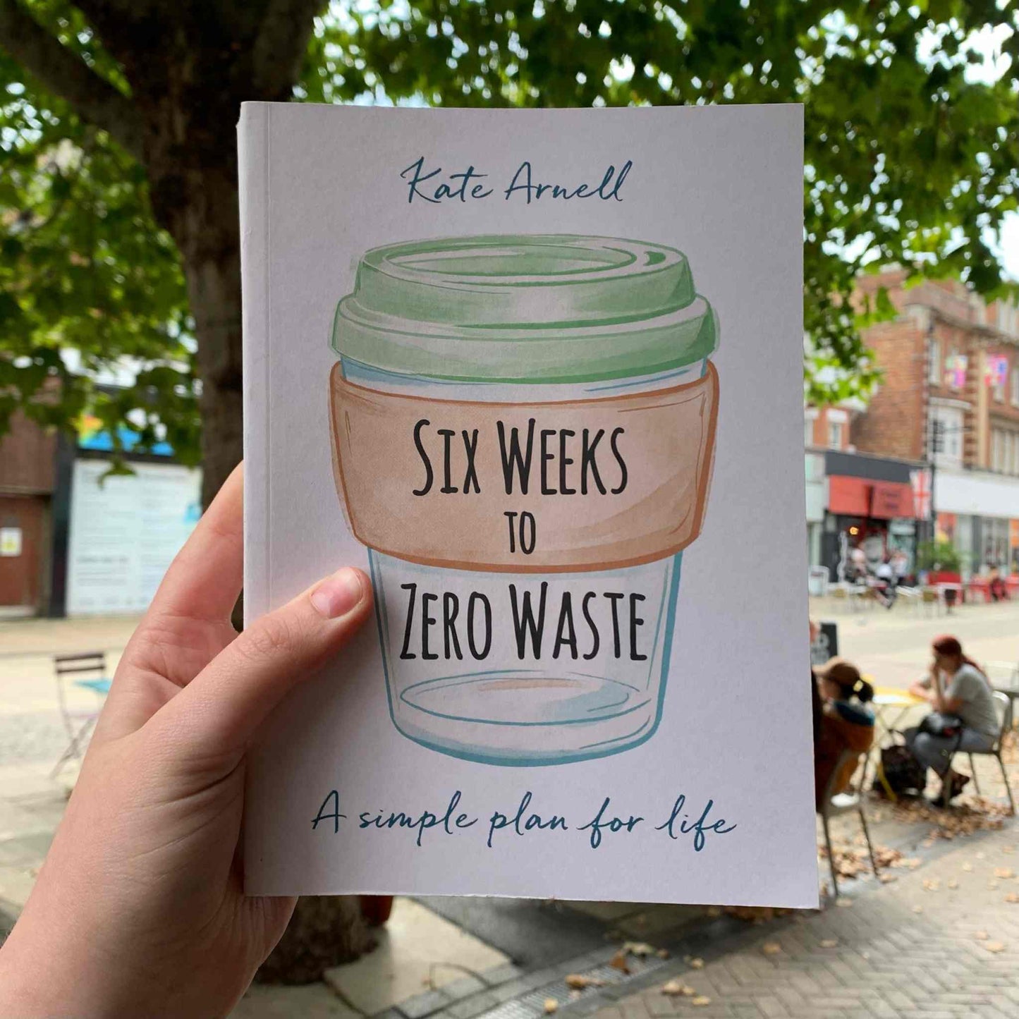 Holding the book "Six Weeks to Zero Waste" by Kate Arnell outdoors.