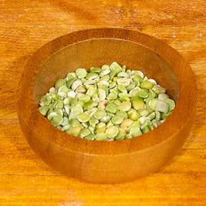 green split peas in a wooden bowl on a wooden surface