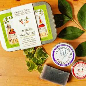 Gift tin with lavender and rose set by Filberts of Dorset, featuring lavender salve, soap, and other aromatherapy products on a wooden surface.