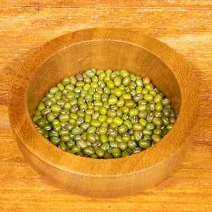 Mung beans in a wooden bowl on a wooden surface.
