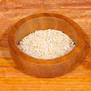 Orzo pasta in a wooden bowl on a wooden surface.