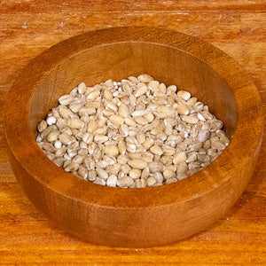 Pearl barley (100g) in a wooden bowl on a wooden surface.