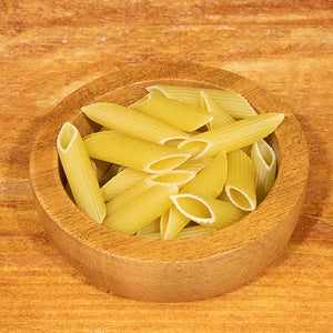 Penne rigate in a wooden bowl on a wooden surface, 100g package.