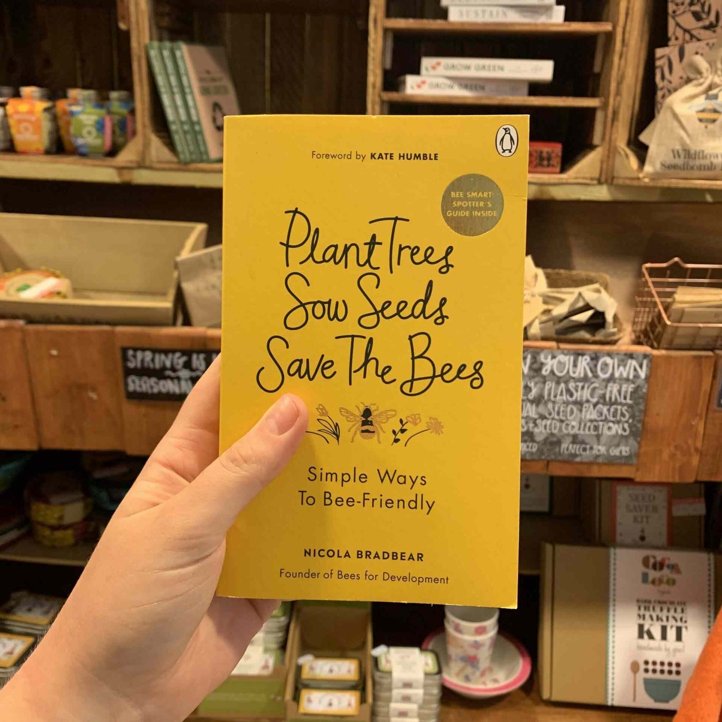 "Plant Trees, Sow Seeds, Save the Bees" book by Nicola Bradbear held in a hand, promoting eco-friendly practices.