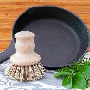 Eco-friendly wooden pot brush with natural bristles beside cast iron pan.