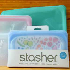 Stasher food pouches, eco-friendly silicone bags in various colors, displayed on a wooden surface.