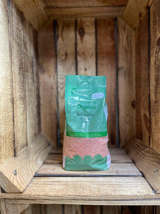 Organic Red Football Lentils in green packaging on a wooden shelf.