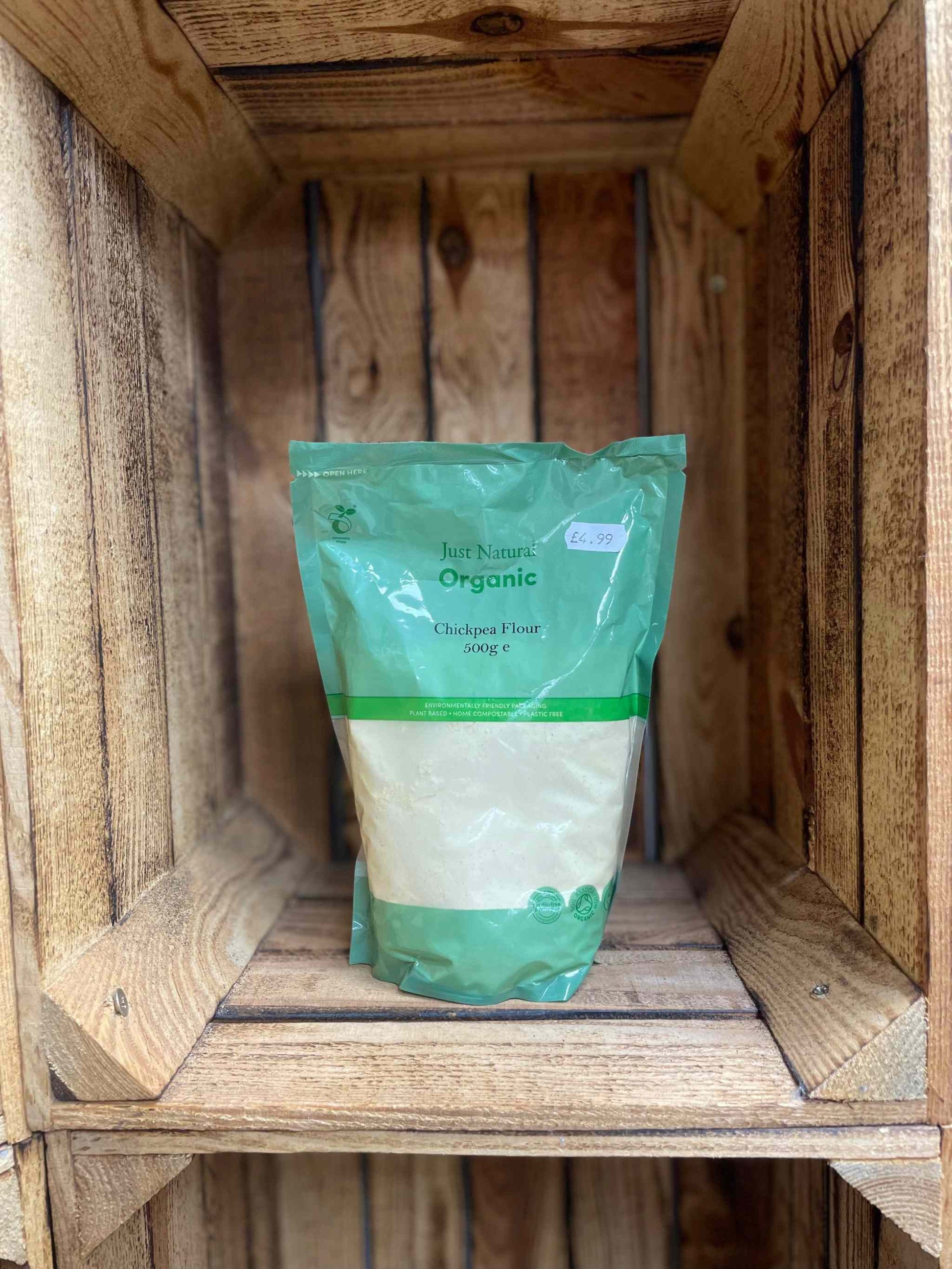 Organic chickpea flour 500g in green packaging on wooden shelf.