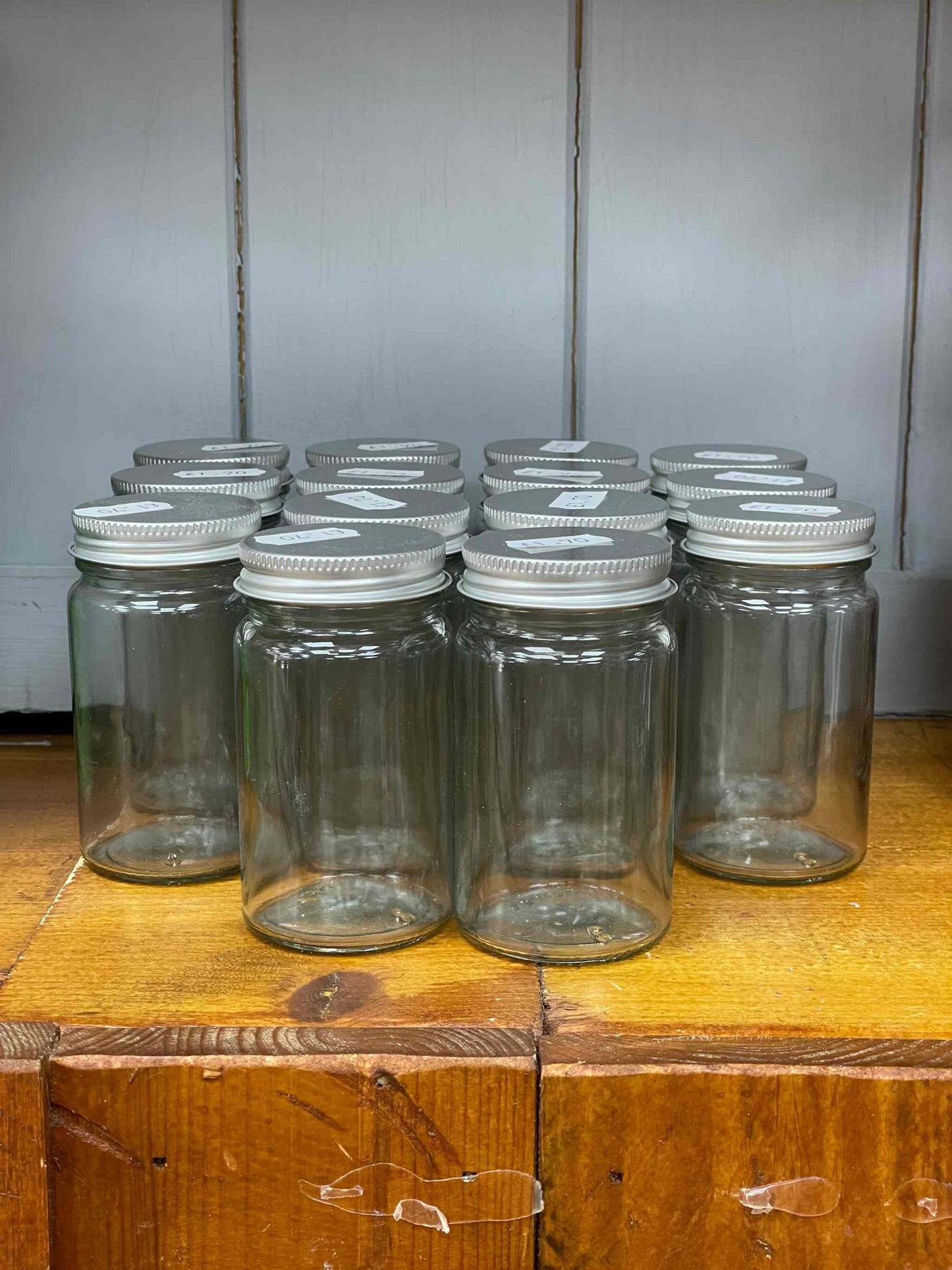 Clear glass spice jars with silver screw top lids displayed on a wooden surface.