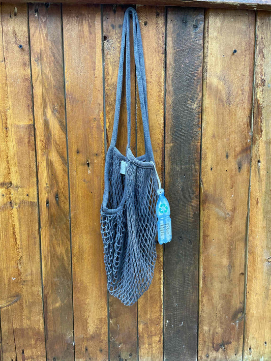 Eco-friendly long handle string bag in charcoal hanging on a wooden wall.