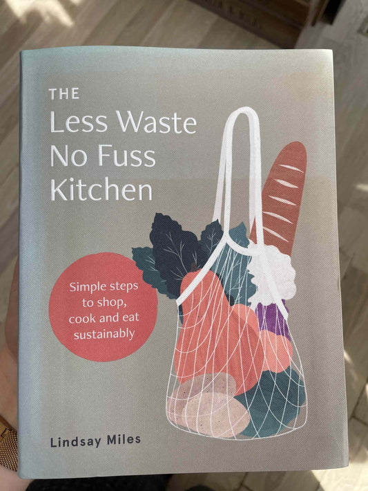 The Less Waste No Fuss Kitchen book cover displaying a reusable bag with groceries, promoting sustainability.