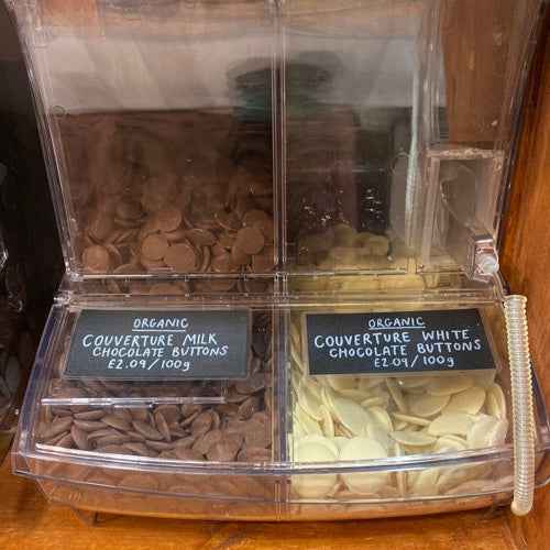 Organic couverture milk and white chocolate buttons in bulk containers.